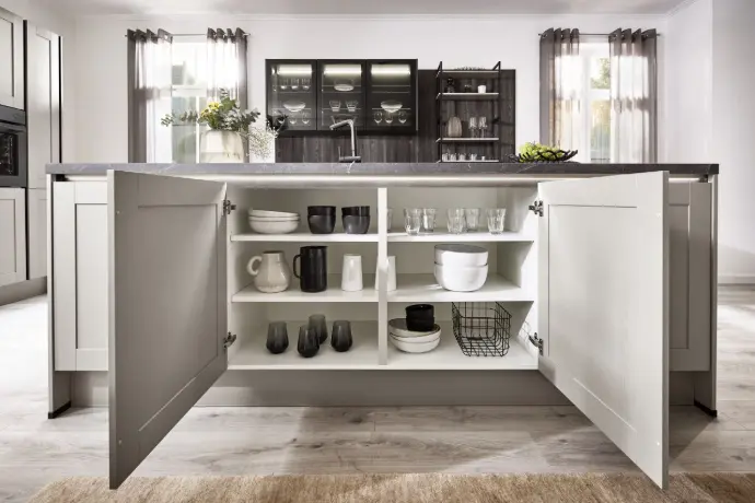 Offene Kücheninsel mit geöffneter Front und großzügigem Stauraum. Geschirr, Gläser und Schalen ordentlich arrangiert – modernes Landhausdesign mit klarer Struktur und Funktionalität.
