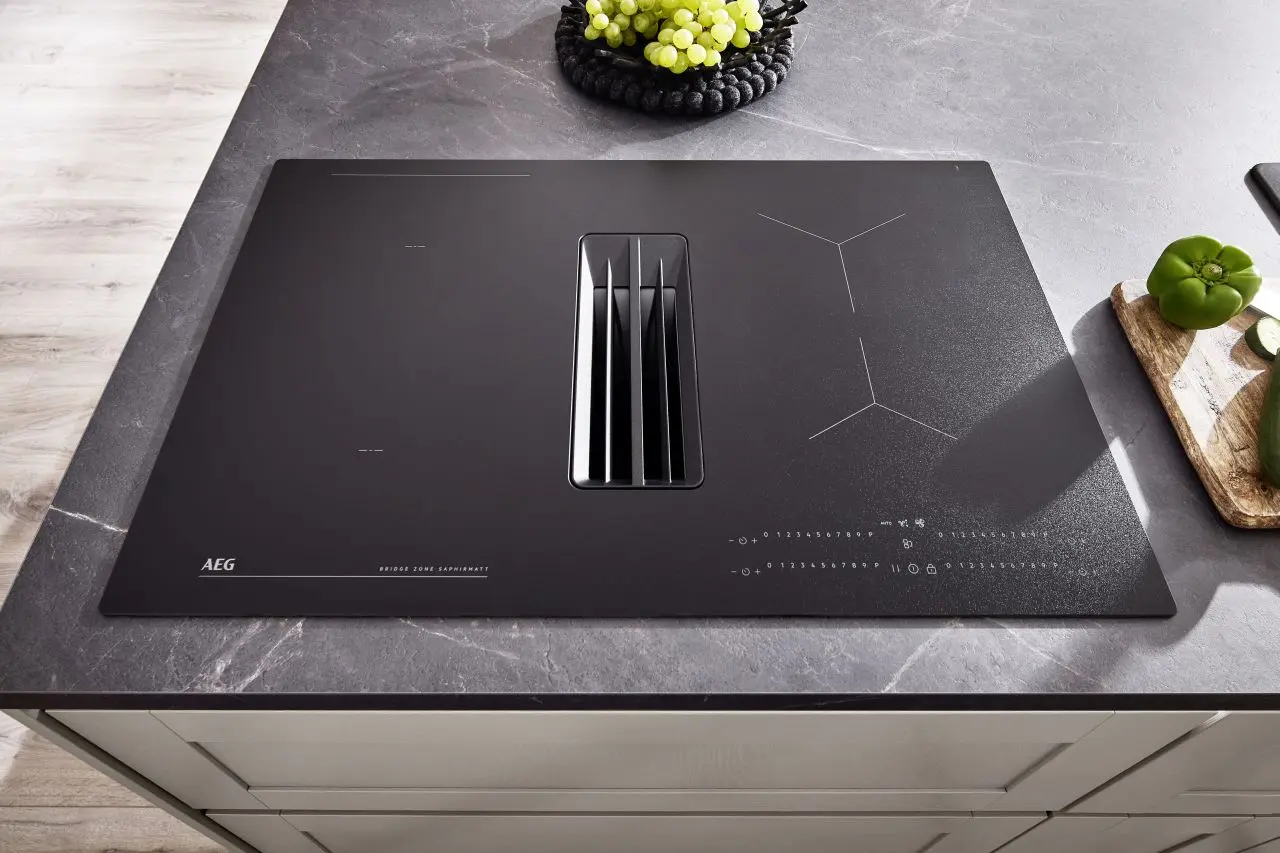 Modernes Induktionskochfeld mit integriertem Kochfeldabzug in schwarzem Glasdesign. Elegante Arbeitsplatte mit natürlicher Marmorstruktur – stilvolles Detail einer hochwertigen Küche.
