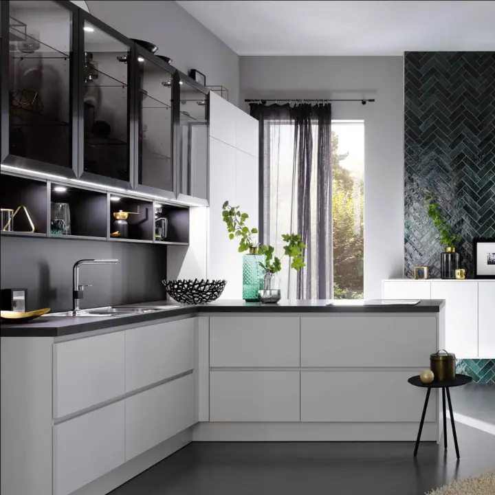 Moderne grifflose L-Küche in Mattweiß mit dunkler Arbeitsplatte, Glasoberschränken und dunkelgrüner Fischgrät-Rückwand – Planung von LS Küchen Wohnen & Service.