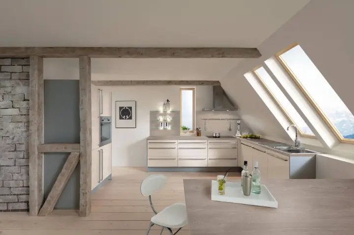 Helle Dachgeschossküche mit großen Dachfenstern, sichtbaren Holzbalken, sandfarbenen Fronten und moderner L-Form Planung von LS Küchen.