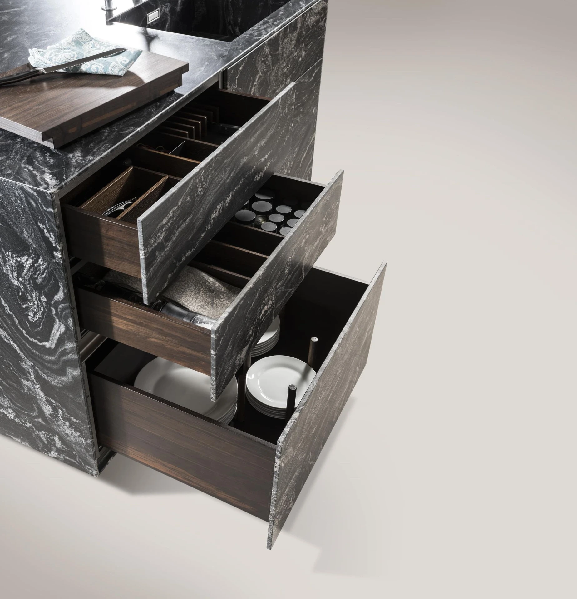 Geöffnete Küchenauszüge in einer Insel mit dunkler Natursteinverkleidung; innen sind Besteck, Gewürze und Geschirr in dunklen Holzeinsätzen übersichtlich organisiert.