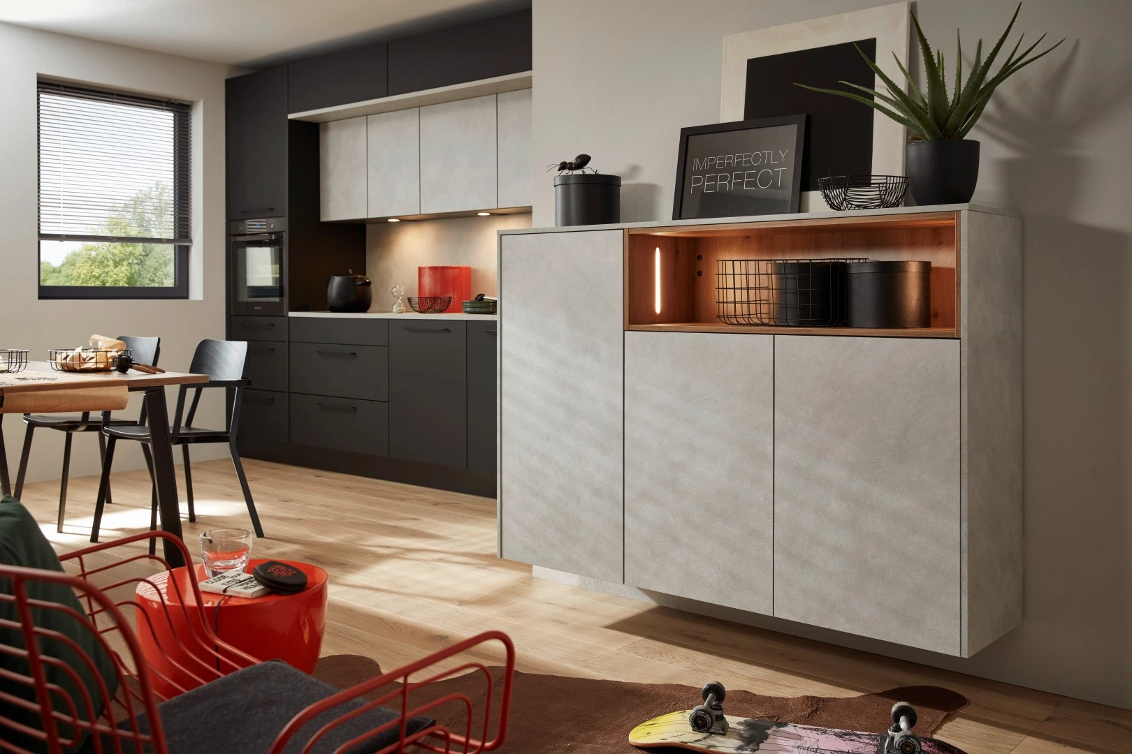 Moderne Wohnküche mit matten anthrazitfarbenen Fronten, hellen Betonoptik-Fronten und Holzregal mit warmem Licht.